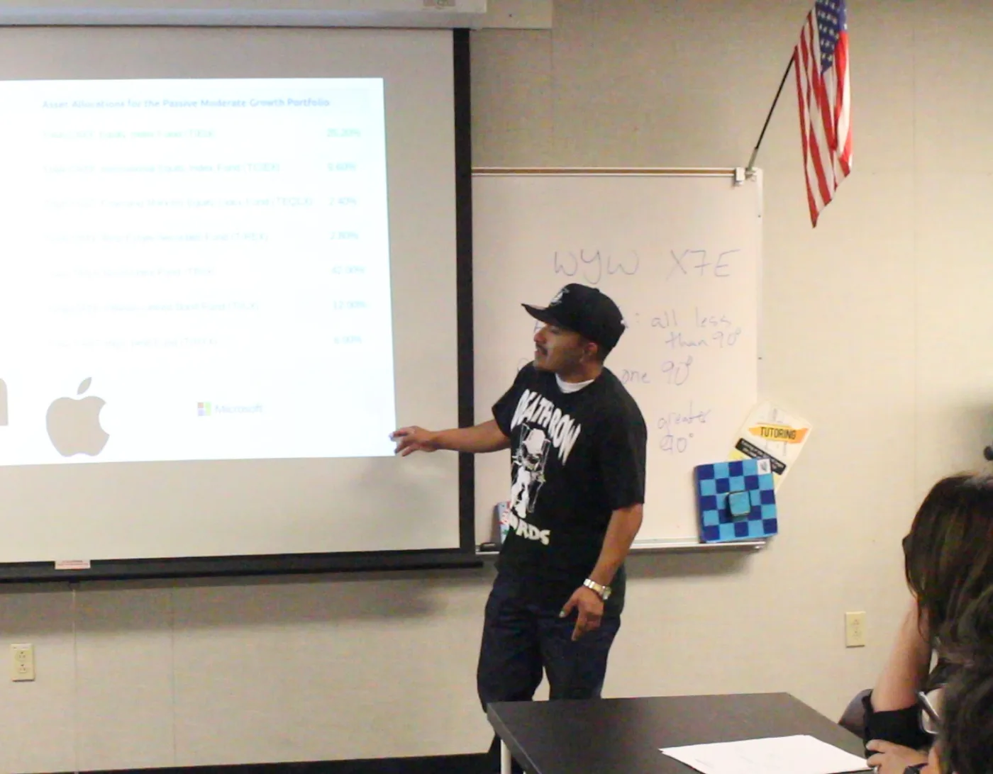 Eulises stands at the projector presenting his own asset allocation to the class